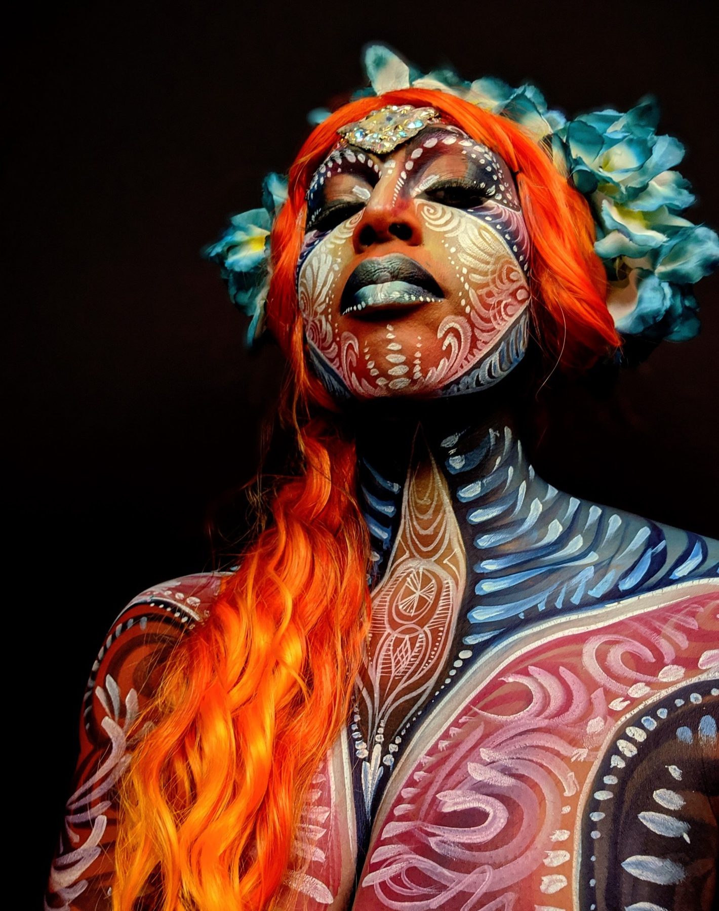 Model bodypainted in coral and blue patterns with flowing orange hair